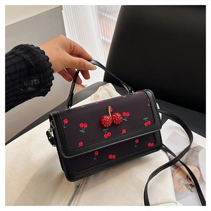 Detailed close-up of a black leather handbag featuring 3D cherry buckle and cherry prints