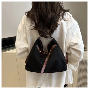 Detail of black tote bag featuring brown leather straps and metal buckles on white shirt