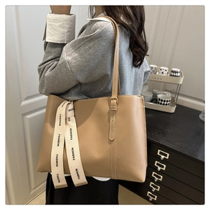 Detail of khaki tote bag with adjustable strap and decorative 'FASHION' ribbon accent