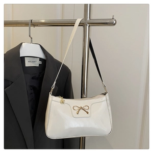 Detail of cream patent leather bag with gold bow and floral pendant on shoulder strap