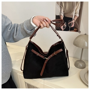 Detail of a large black suede tote bag with brown leather straps in a home setting