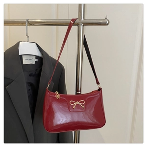 Close-up of red patent leather shoulder bag featuring gold bow and floral metal accents