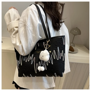 Detail of embroidered wavy patterns on a black canvas tote bag with a plush charm