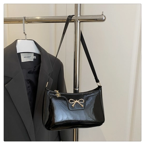Detail of black patent leather bag with gold bow charm against a blazer background