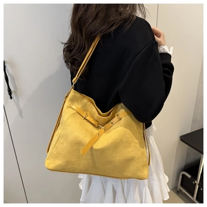 Detail of a bright yellow suede tote bag featuring metallic buckles and a side-view silhouette