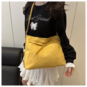 Detail of yellow suede tote bag with leather straps and metal buckle shown on model