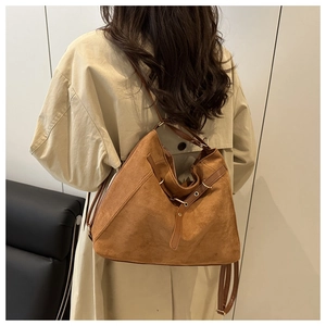 Close-up of caramel brown suede hobo bag with leather straps on a person's shoulder