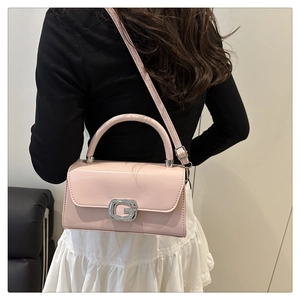 Pink crossbody bag with silver G buckle shown on a model in a minimalist home setting