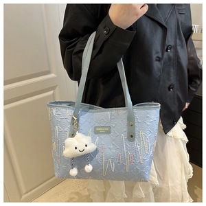 Dettaglio della borsa tote azzurra a rilievo con logo dorato e ciondolo a nuvola