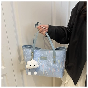 Dettaglio della borsa tote azzurra con ricamo ondulato e charm a nuvola bianca
