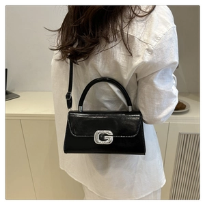 Detail of a black glossy leather square handbag with silver rhinestone G buckle on a model