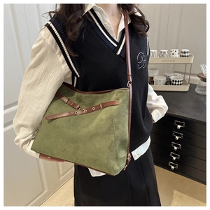 Olive green suede tote bag with brown leather accents shown on a model in a minimalist room
