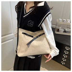 Detail of beige suede tote bag with black buckle strap shown on model in cozy home setting