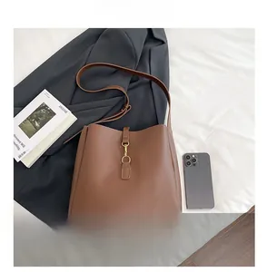 Brown bucket style shoulder bag with gold clasp shown next to a phone for size scale