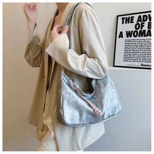 Close-up of a silver metallic shoulder bag with a woven tassel charm worn by a model