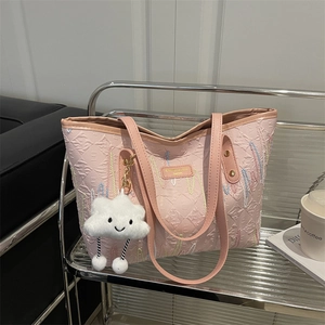 Borsa tote rosa con ricami e ciondolo a nuvola su un ripiano per arredamento