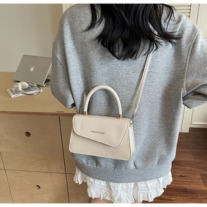 Detail of beige textured shoulder bag with golden buckle and woven finish on model