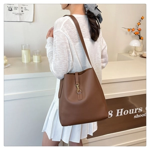 Close-up of caramel brown leather bucket bag with gold metal buckle and long strap