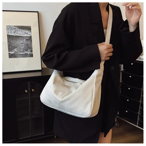 Model wearing a textured ivory crescent tote bag with wide shoulder strap and zipper