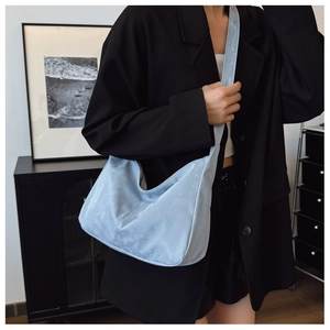Detail of light blue suede hobo bag with seamless strap worn by a model in a blazer