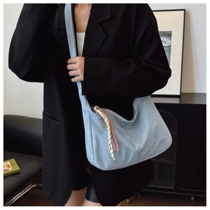 Detail of light blue suede tote bag with woven fringe pendant and metal nameplate