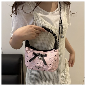 Detailed close-up of pink embossed crossbody bag with bow, heart charm and chain strap