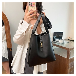 Close-up of black leather bucket bag with a golden metal buckle and wide shoulder strap
