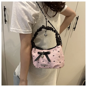 Detail of pink embossed shoulder bag with black bows and silver heart charm pendant