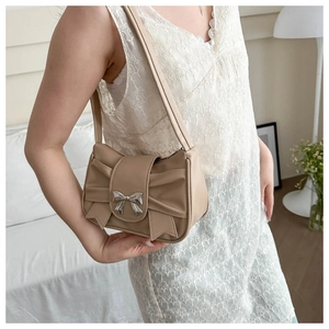 Detailed view of the pleated bow design and silver metal buckle on a beige shoulder bag