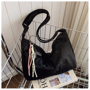 Detail of black suede hobo bag with woven charm and silver abacus tag in a metal basket