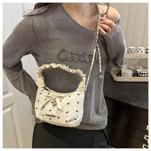 Detail of white textured shoulder bag featuring black bow prints and metal chain strap