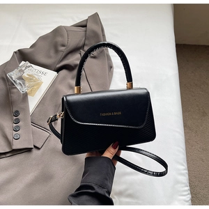 Detail of black crossbody bag with gold text on premium leather placed on a grey blazer