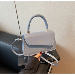 Detailed view of grey-blue crossbody bag with textured weaving and gold lettering