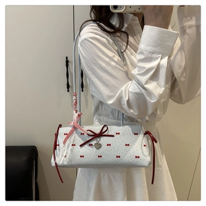 Sac sous le bras blanc chic avec motifs de nœuds rouges et pendentif cœur porté par un modèle