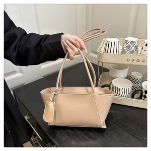 Close-up of minimalist beige handbag featuring elegant thin handles and square bag charm