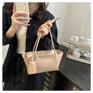 Detail of beige faux leather handbag with stitching, top handle and matching tag accessory