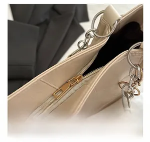 Detail shot of golden metal zipper and round handle buckle on cream faux leather tote bag