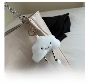 Detail of white fluffy cloud plush charm with striped legs hanging on a leather shoulder bag