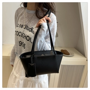 Détail d'un sac cabas en cuir noir mat minimaliste avec bandoulière et pendentif