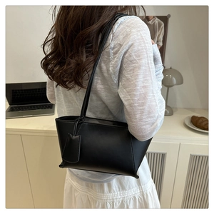 Grand cabas minimaliste en similicuir noir porté à l'épaule dans un décor de bureau chic