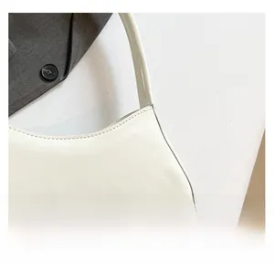 Detailed close-up of glossy white patent leather finish and stitching on shoulder bag
