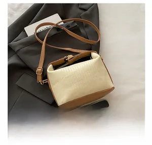 Detail of ruched beige fabric bag with brown leather base and adjustable shoulder strap