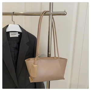 Detail of beige minimalist faux leather tote bag hanging on a rack with long strap