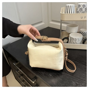 Detail of cream pleated handbag with brown leather handles and golden metal clasp