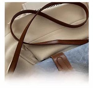 Detail of adjustable blue denim strap with brown leather trim and golden metal buckle