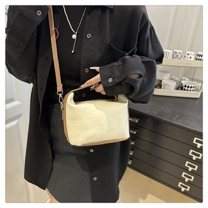 Close-up of cream textured crossbody bag with brown leather trim and gold metal hardware