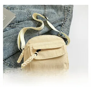 Detail of corduroy crossbody bag with dual zipper pulls on denim jacket background