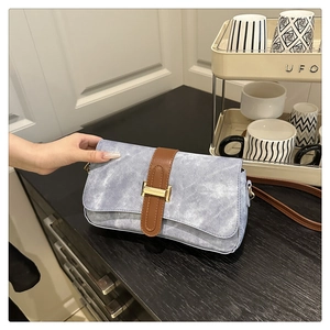 Detail of light blue denim shoulder bag with brown leather strap and gold buckle hardware