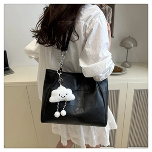 Detail of a black leather tote bag with geometric stitching and cloud plush charm