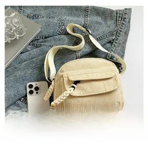 Detail of beige corduroy crossbody bag with woven zipper pull over a denim jacket